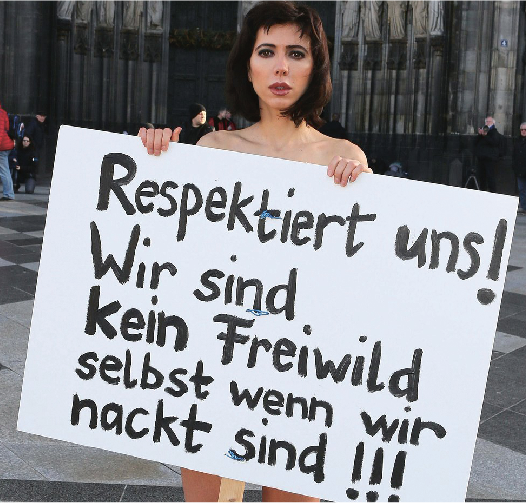 ‘Respect Us! We are not fair game even when naked!!!’ read a simply painted protest sign created by Milo Moire on Friday. The Swiss artist wore the sign and little else during her performance in front of the Cologne Cathedral on Friday, which was a nude protest against sexual assault in the city.